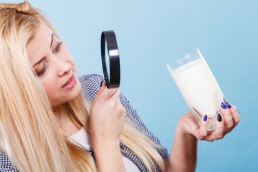 Frau untersucht ein Glas Milch mit der Lupe