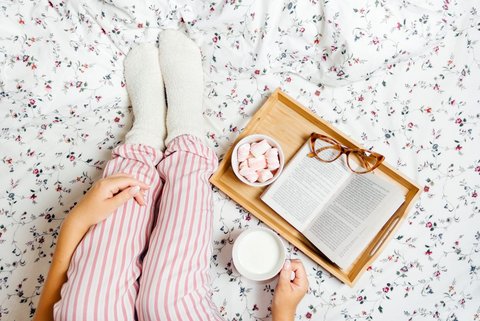 Frau sitzt auf dem Bett mit einem Tablett und einer Tasse Milch