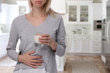 Frau fasst sich an den Bauch und hält ein Glas Milch in der anderen Hand