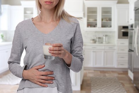 Frau fasst sich an den Bauch und hält ein Glas Milch in der anderen Hand