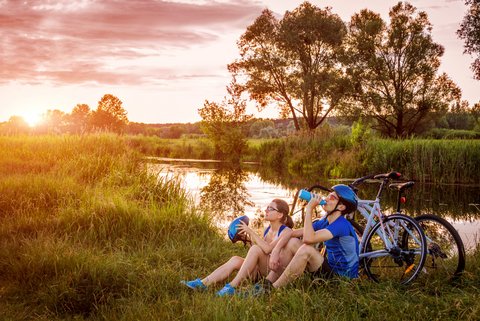 Zwei Radfahrer machen Trinkpause an einem Fluss