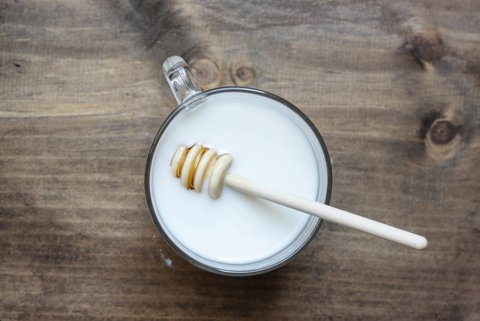 Eine Tasse Milch mit Honiglöffel